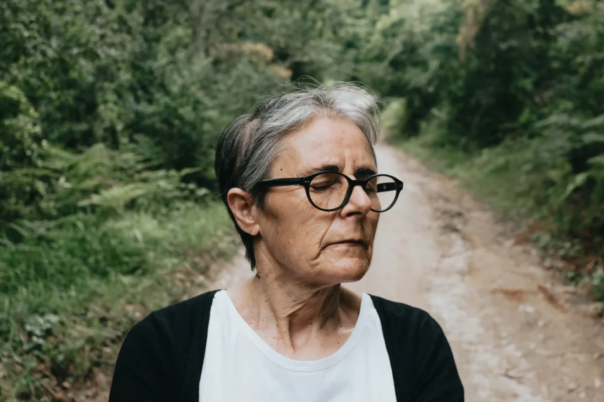 Starší žena je v lese a tváří se udiveně.