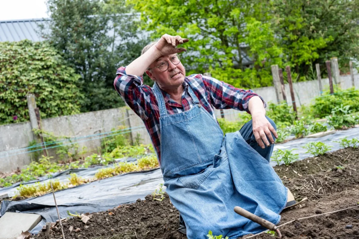 Starý člověk klečí na poli a utírá si pot z čela.