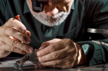 detail - hodinář při práci, sklání se (šedovlasý) nad hodinkami u stolu