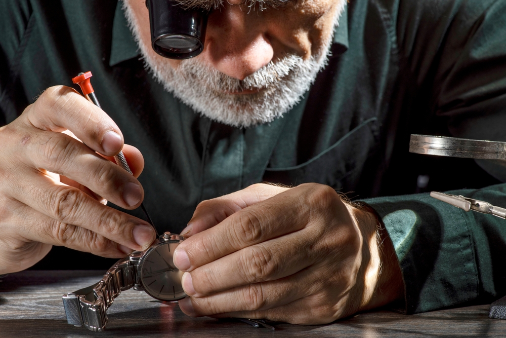 shutterstock_25421065272 | TVGURU.cz detail - hodinář při práci, sklání se (šedovlasý) nad hodinkami u stolu