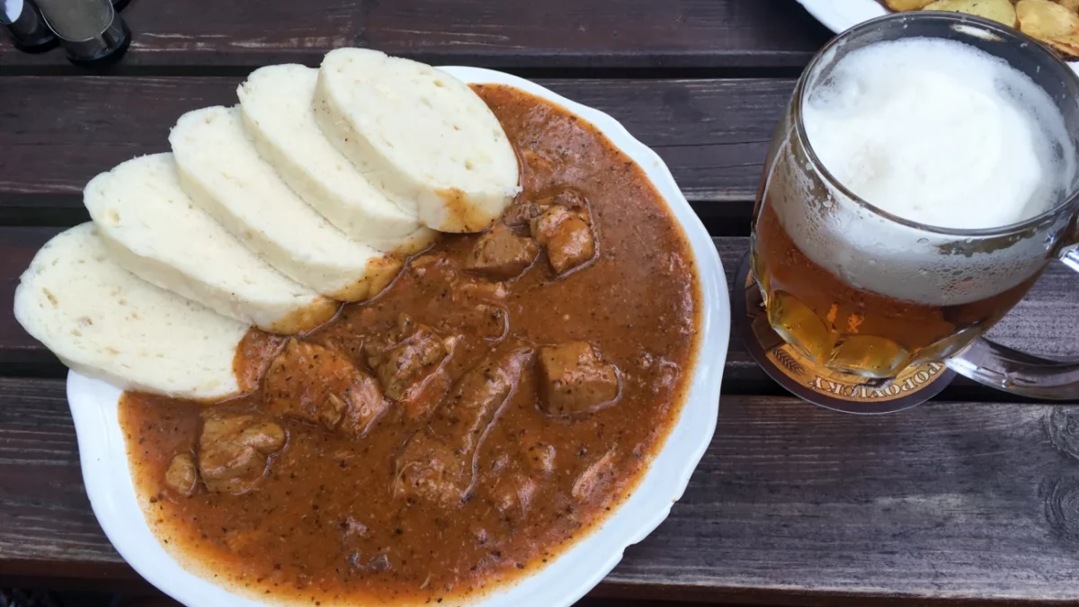 Bílý talíř s gulášem a knedlíkem + pivem na dřevěném stole