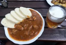 Bílý talíř s gulášem a knedlíkem + pivem na dřevěném stole