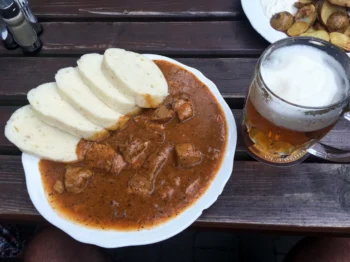 Bílý talíř s gulášem a knedlíkem + pivem na dřevěném stole