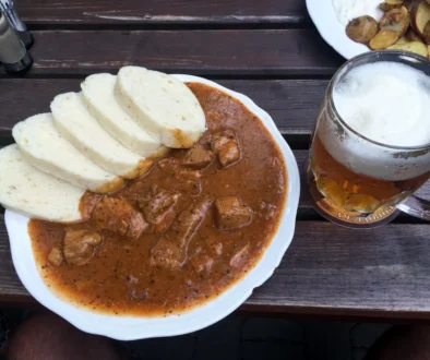 Bílý talíř s gulášem a knedlíkem + pivem na dřevěném stole