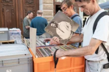 Lidé venku na bleším trhu zkoumají nabídku gramodesek v krabicích