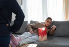 Slečna leží na gauči a míří ovladačem na televizi.