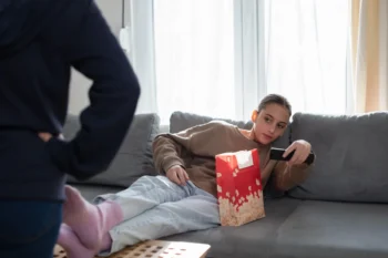 Slečna leží na gauči a míří ovladačem na televizi.