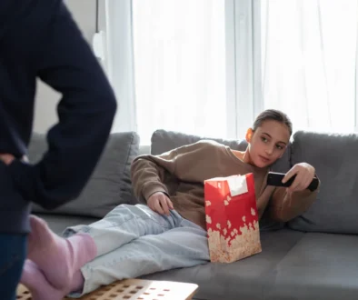 Slečna leží na gauči a míří ovladačem na televizi.