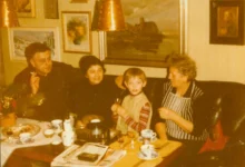 Retro foto ze 70.-80. let. Rodinná party v obýváku (5 lidí na pohovce u stolku, za nimi na zdech obrazy)