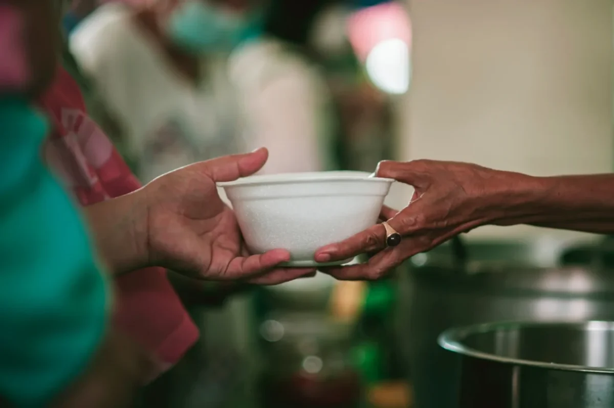 žena podává druhé ženě misku s polévkou, záběr na ruce