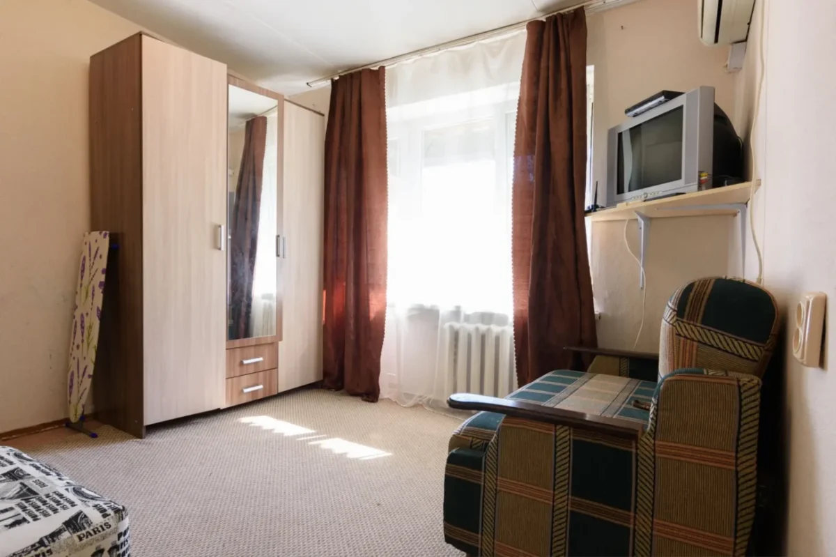 fotka skromného bytu s televizí, křeslem a skříní