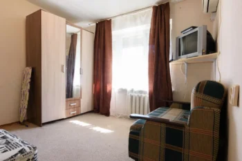 fotka skromného bytu s televizí, křeslem a skříní