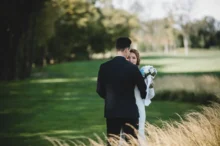 Nevěsta s ženichem stojící na louce v objetí.