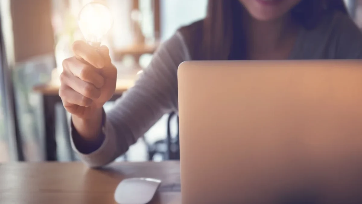 Žena sedí u notebooku a v ruce drží žárovku.