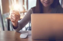 Žena sedí u notebooku a v ruce drží žárovku.