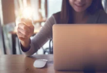 Žena sedí u notebooku a v ruce drží žárovku.