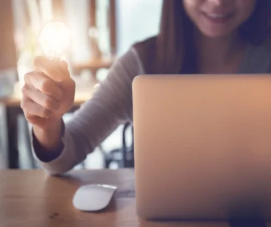 Žena sedí u notebooku a v ruce drží žárovku.