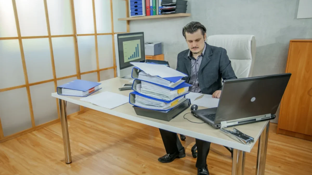 Muž pracuje u stolu a je obklopený notebookem s deskami.