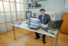 Muž pracuje u stolu a je obklopený notebookem s deskami.