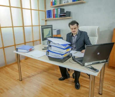 Muž pracuje u stolu a je obklopený notebookem s deskami.