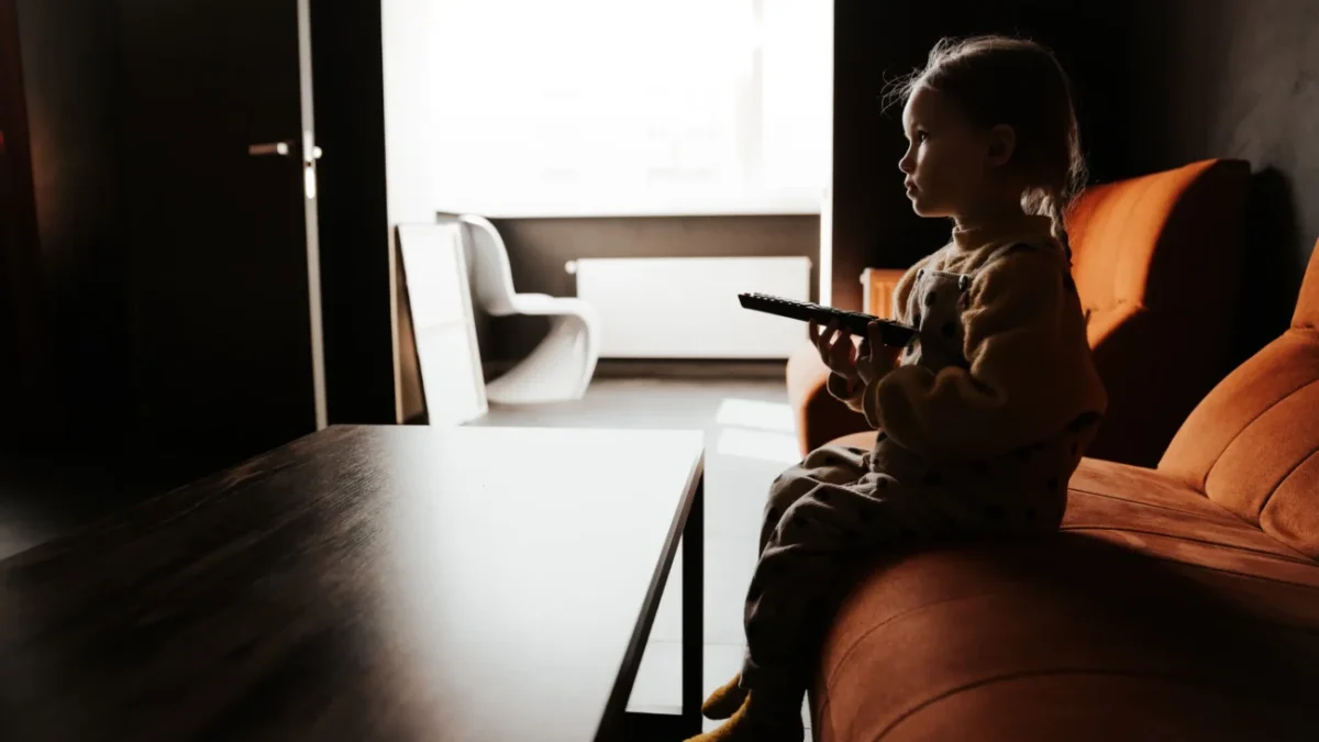 Holčička sedí ve tmě na gauči a dívá se na televizi.