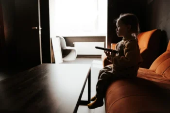 Holčička sedí ve tmě na gauči a dívá se na televizi.