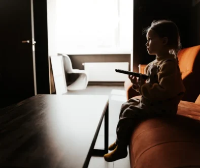 Holčička sedí ve tmě na gauči a dívá se na televizi.