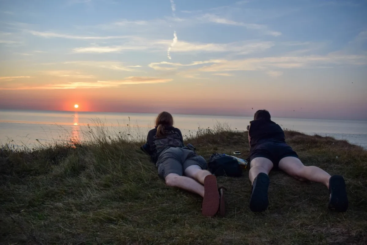 Muži leží na útesu a pozorují západ slunce.