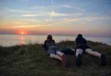 Muži leží na útesu a pozorují západ slunce.