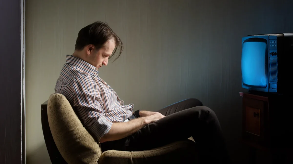 Muž usnul na židli před televizí.