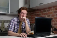 Muž sedí v kuchyni u notebooku.