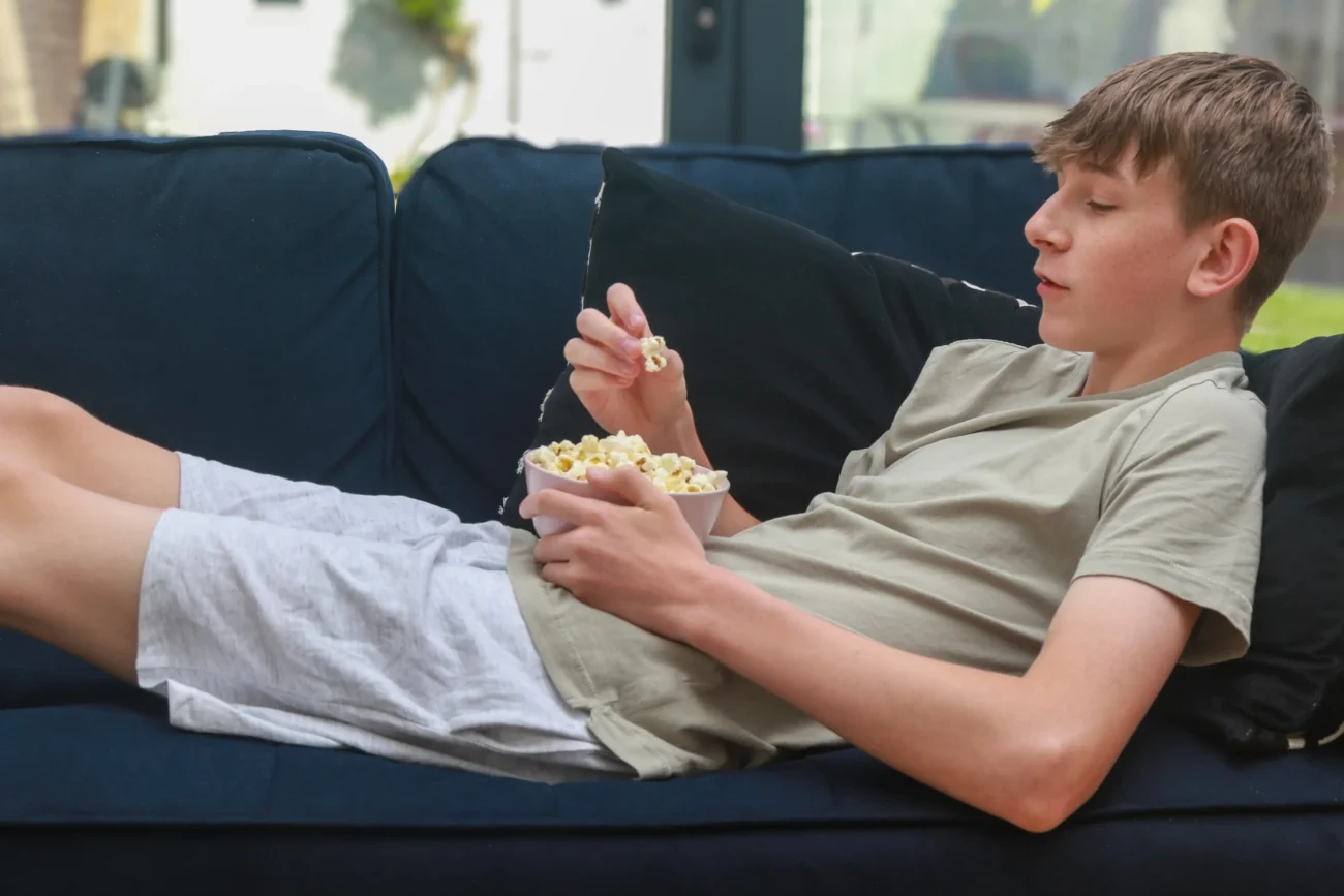 Chlapec leží s mísou popcornu na gauči.