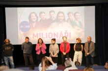 herci ze seriálu Milionáři stojící před plátnem