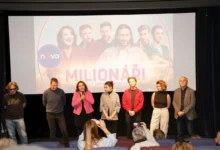 herci ze seriálu Milionáři stojící před plátnem