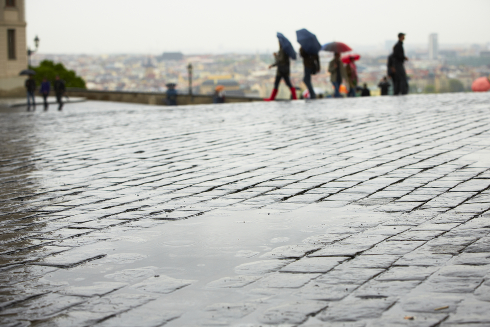 Kaluž na pražské ulici (dlažební kostky, odpoledne, výhled na Prahu)