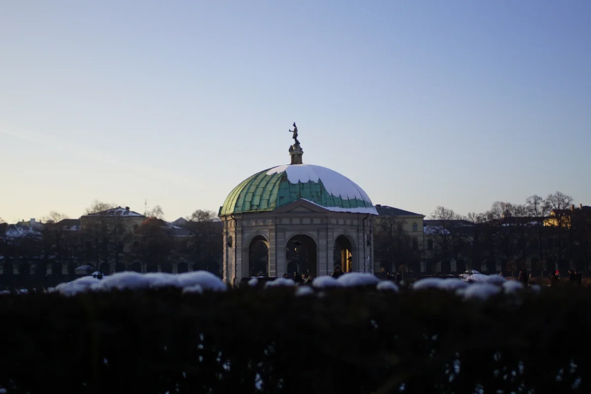 Mnichov, Hofgarten: zimní scéna slavné Zahrady u dvora (Schlossgarten) a Dianina chrámu (Dianatempel) v centru města, s bílým sněhem a modrou oblohou