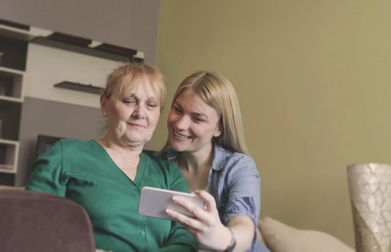 Ženy spolu sedí na gauči a dívají se na telefon. 