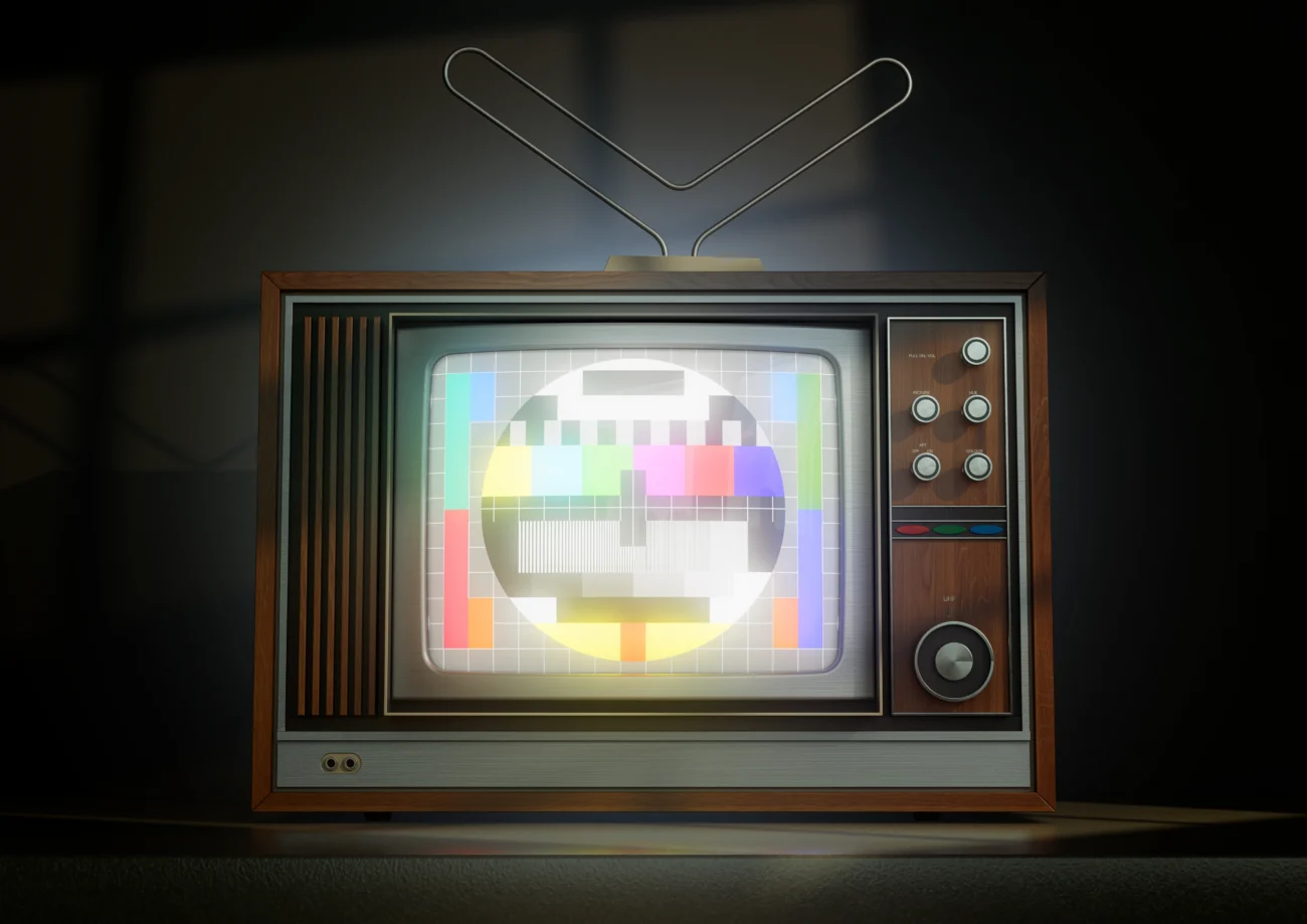 Temná místnost s retro televizorem z 80. let, na jehož obrazovce svítí typický barevný testovací obrazec