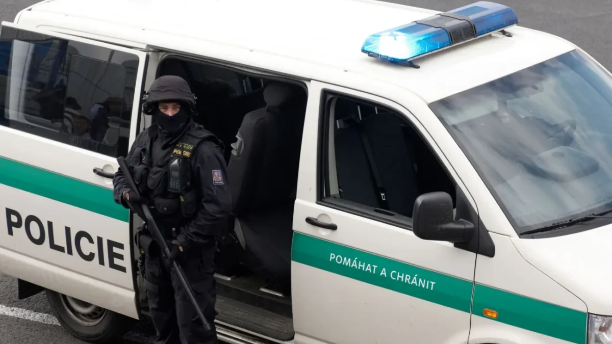 policejní dodávka u které stojí policista s dlouhou palnou zbraní