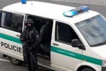 policejní dodávka u které stojí policista s dlouhou palnou zbraní