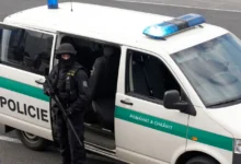 policejní dodávka u které stojí policista s dlouhou palnou zbraní