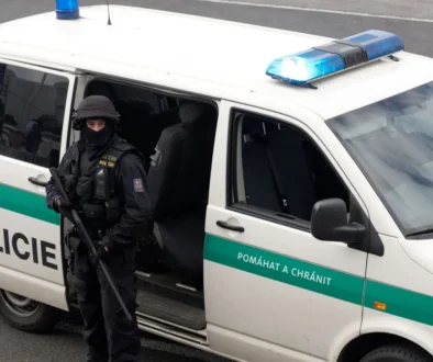 policejní dodávka u které stojí policista s dlouhou palnou zbraní