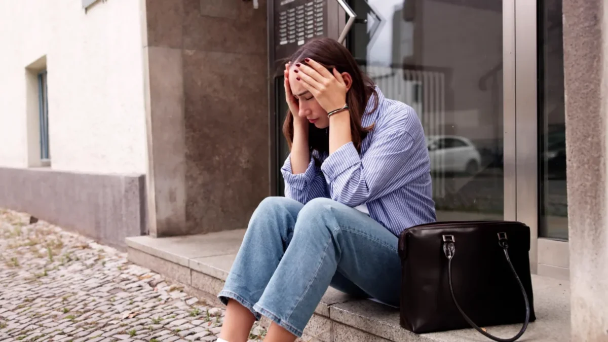 Mladá žena sedí před domem.