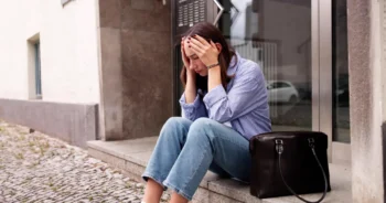 Mladá žena sedí před domem.