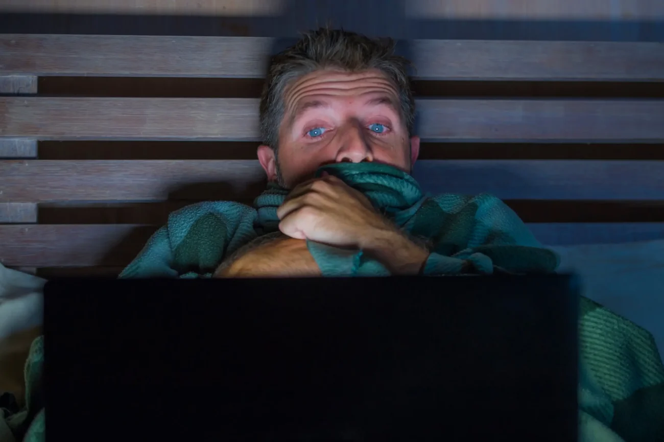 shutterstock_1260704467-2 | TVGURU.cz Muž je schovaný pod peřinou a dívá se na notebook.