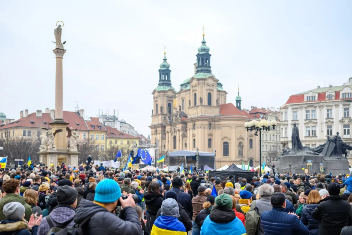 Lidé stojí shromáždění na náměstí.