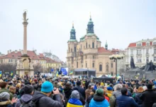 Lidé stojí shromáždění na náměstí.