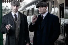 Dva muži stojí na vlakovém nástupišti.