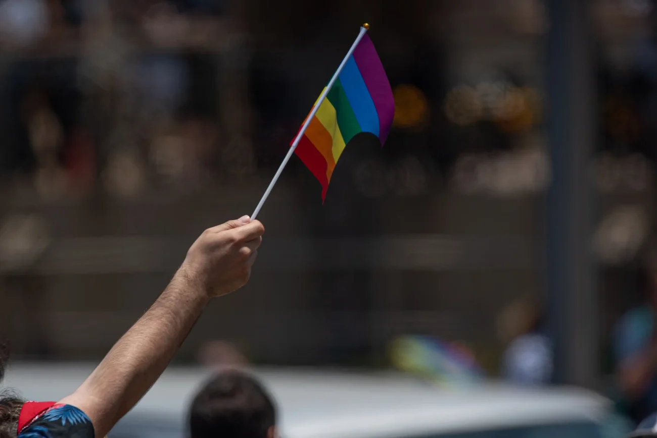 Muž v ruce drží duhovou vlajku.