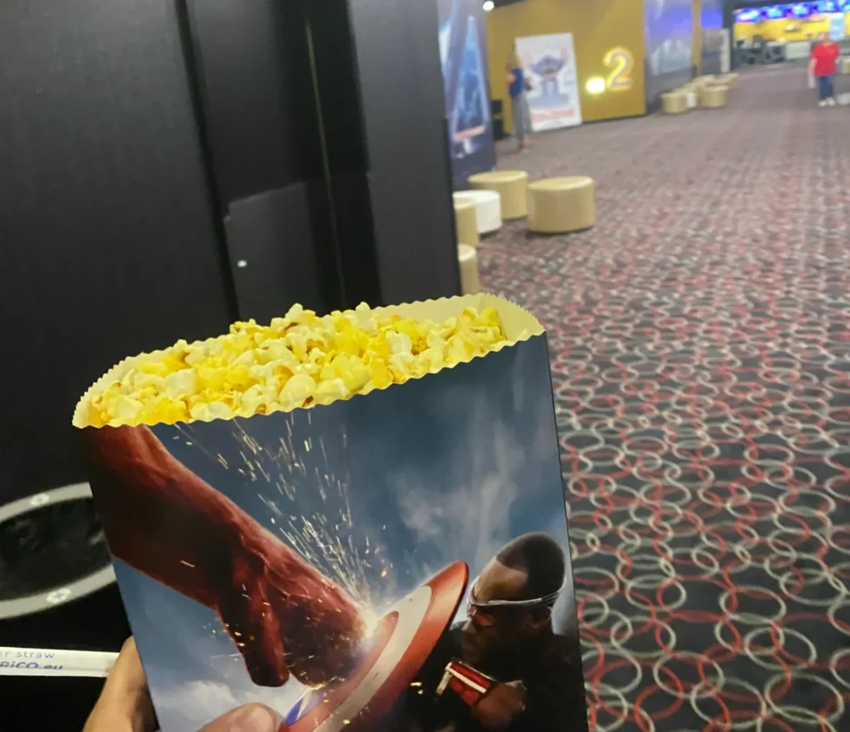 fotografie popcornu v ruce a v pozadí sál kina